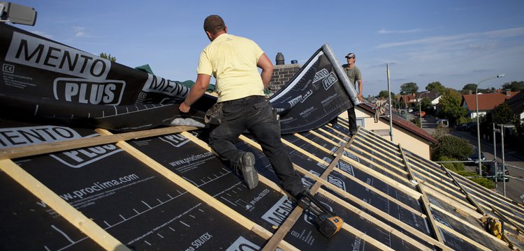 This photograph shows two roofing tradespeople installing SOLITEX Mento Plus membranes on a roof, against a background of a blue sky.